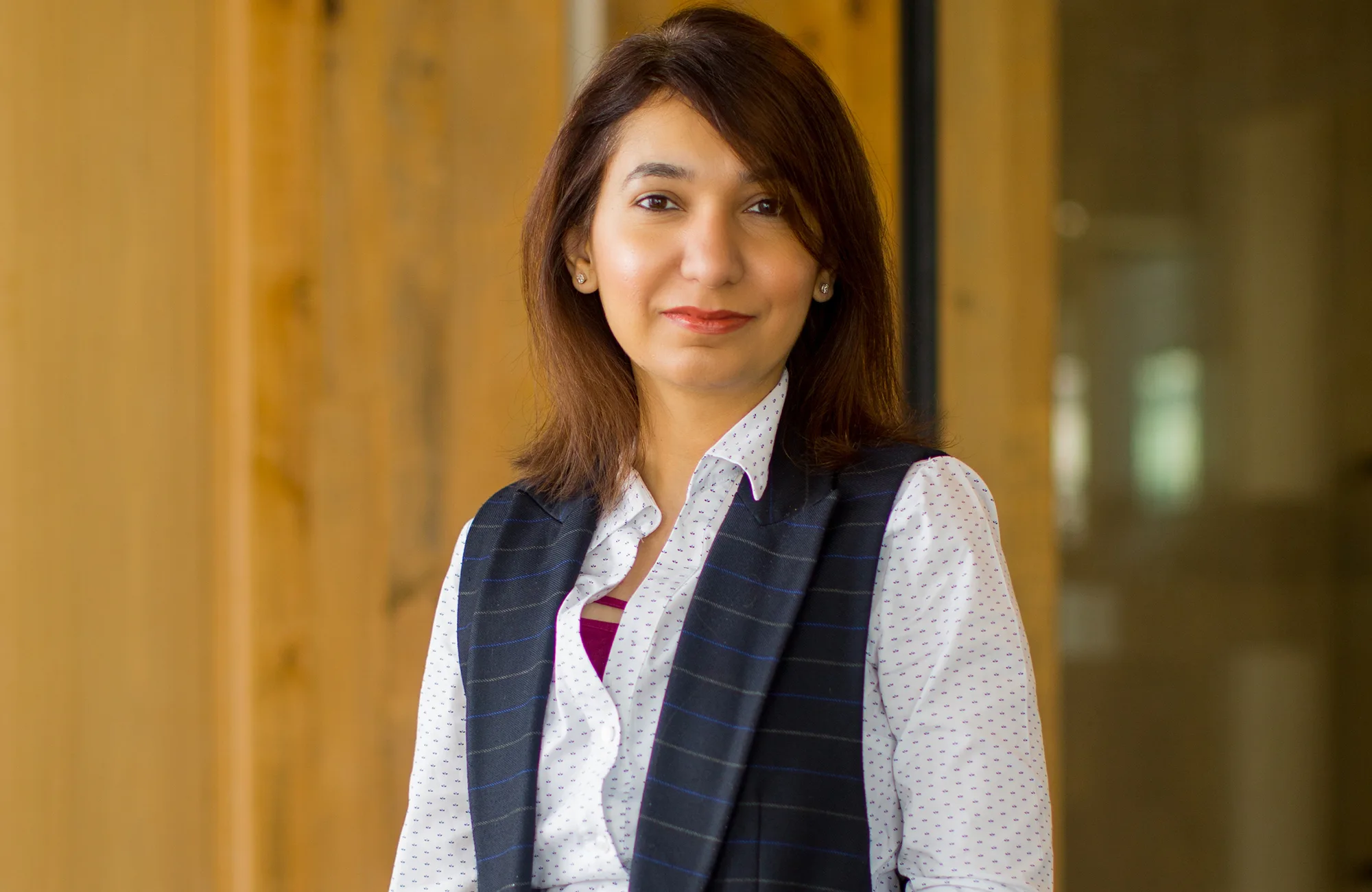 Rabia posing in front of a wooden wall in a white shirt and waistcoat