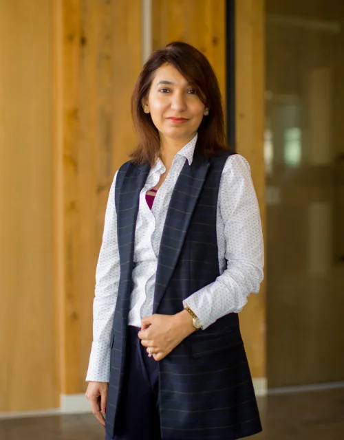 Rabia posing in front of a wooden wall in a white shirt and waistcoat