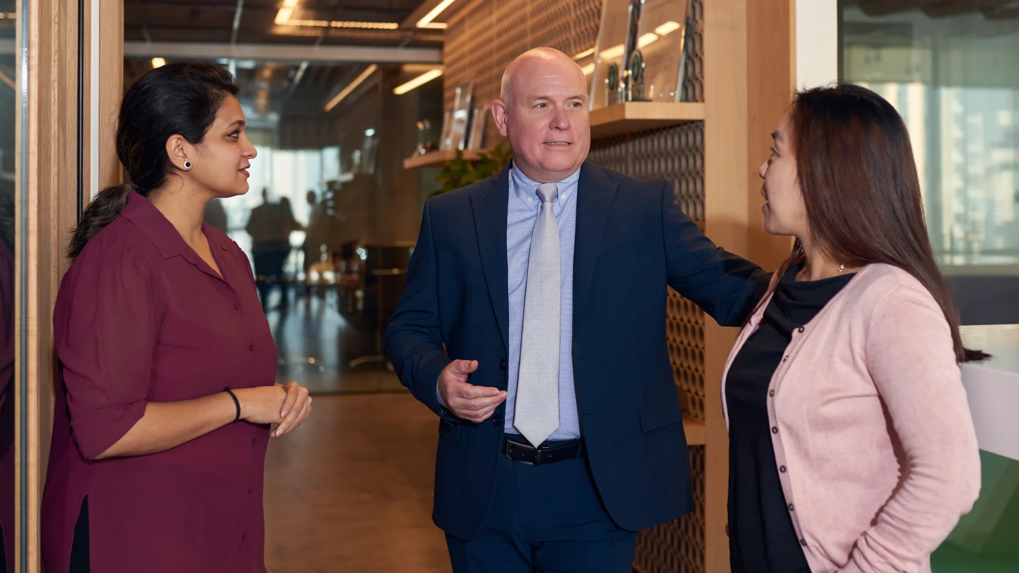 Richard Stratton having a conversation with two female colleagues beside the achievements wall of the Cundall Dubai WELL office