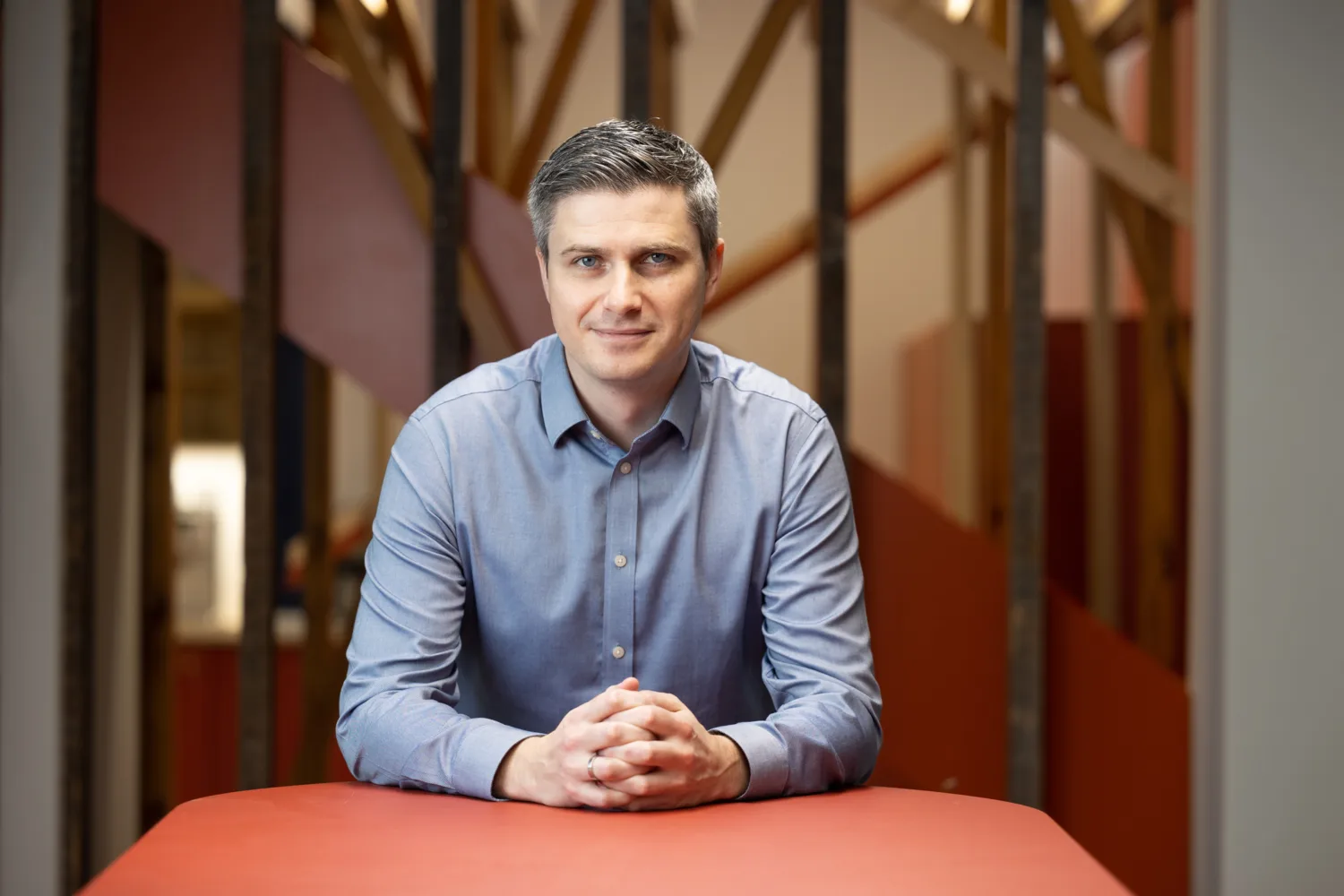 Derry Kearney standing in a blue shirt shirt with his forearms resting on an orange table