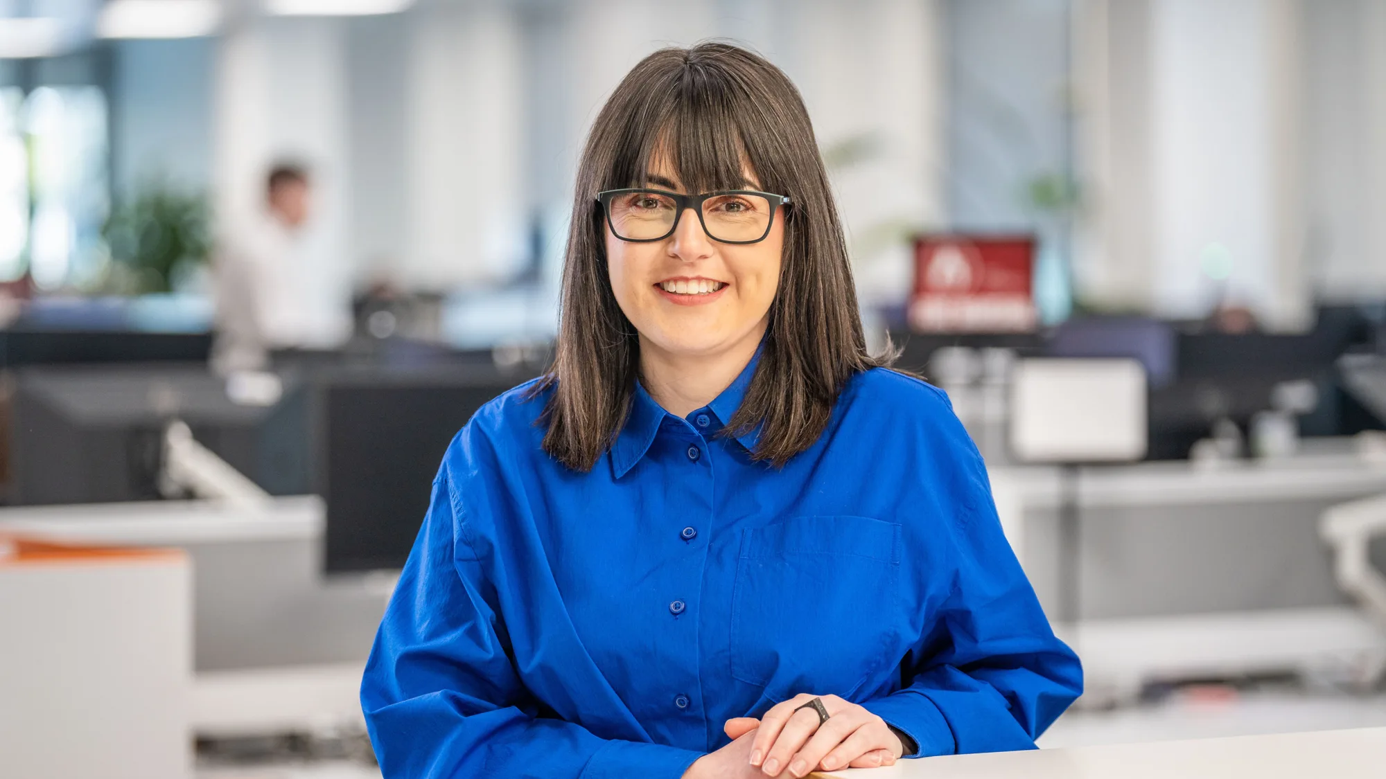 Head and sholders shot of Debbie wearing a blue top leaning on a desk