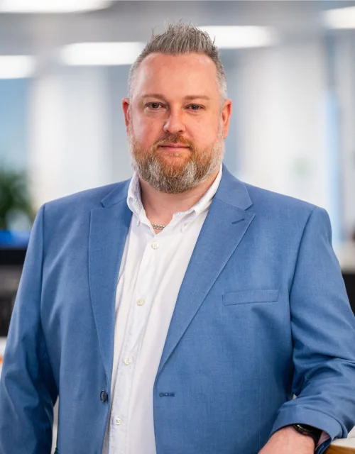 Keith Richardson standing in the Edinburgh office in a white shirt and blue blazer