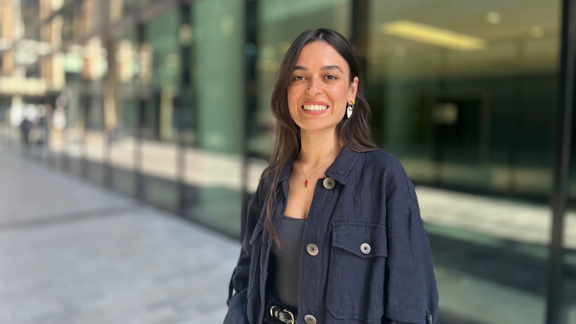 Lucia smiling in front of the glazed office in a large button open collared navy shirt.