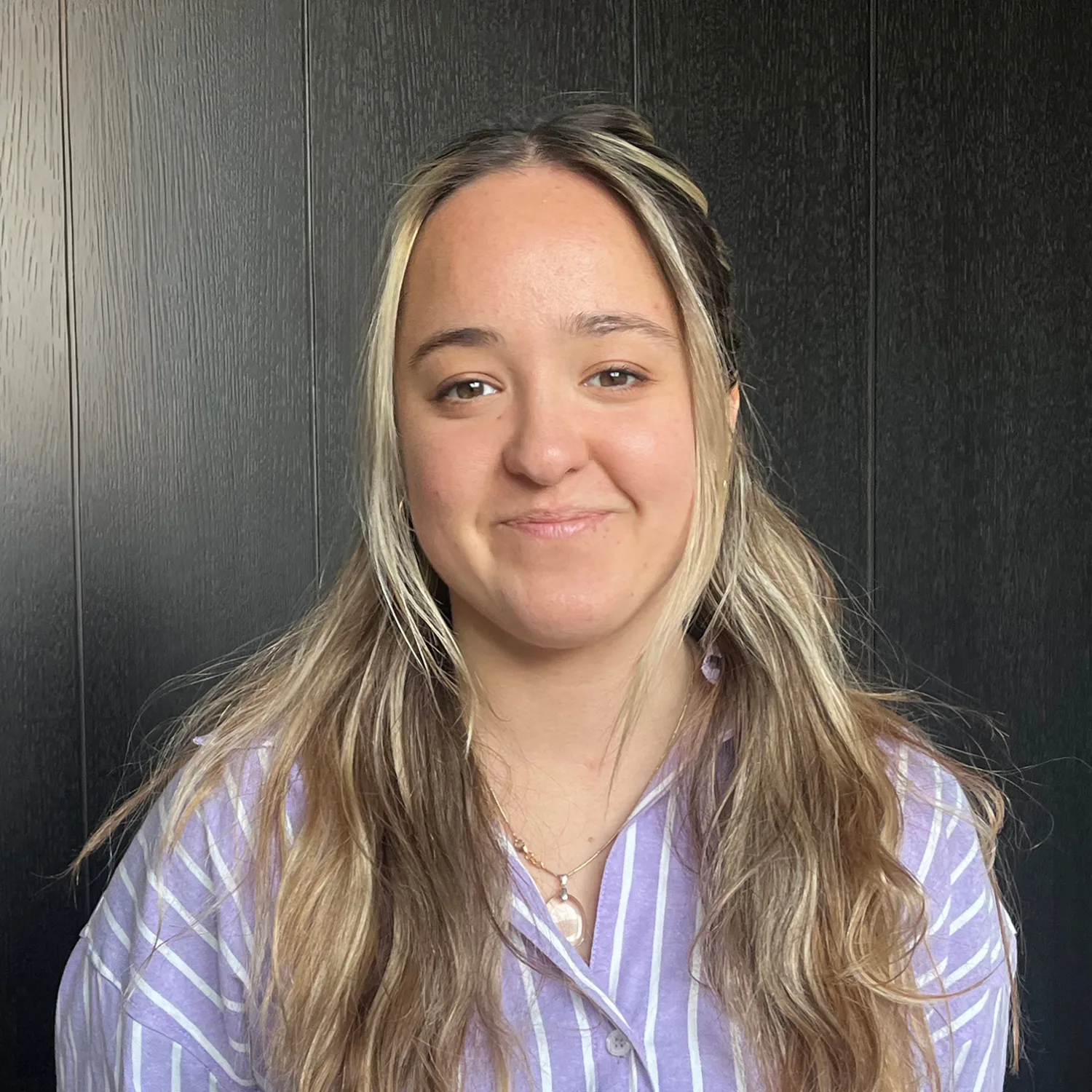 Mia Poppelwell in a blue and white shirt in front of a wooden wall