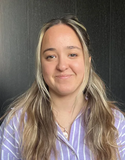 Mia Poppelwell in a blue and white shirt in front of a wooden wall