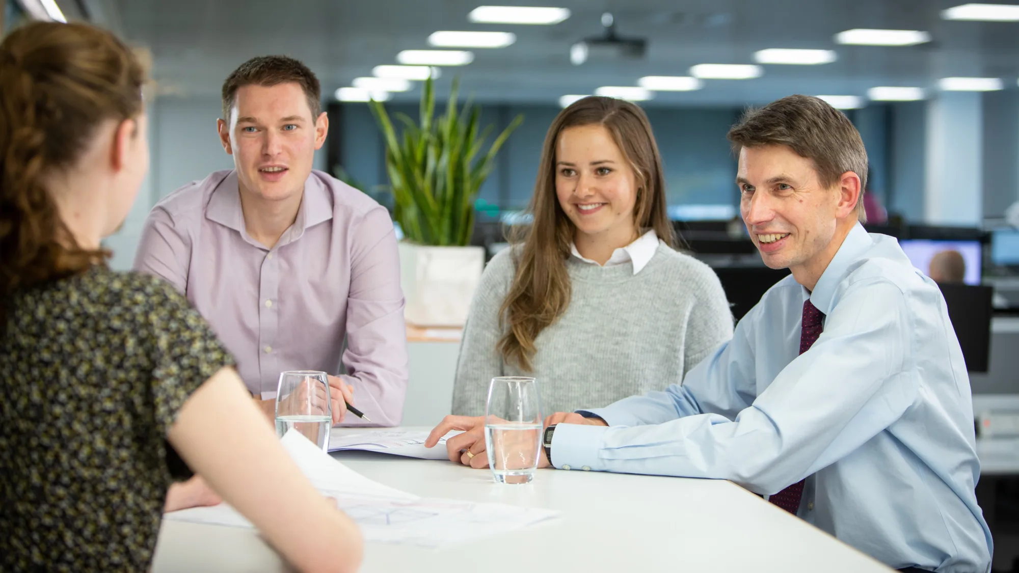 Neil Dely in a meeting with a team of people with planting and office desk area background