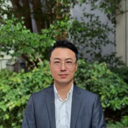 Byeonghee in a shirt and suit jacket looking to camera outside