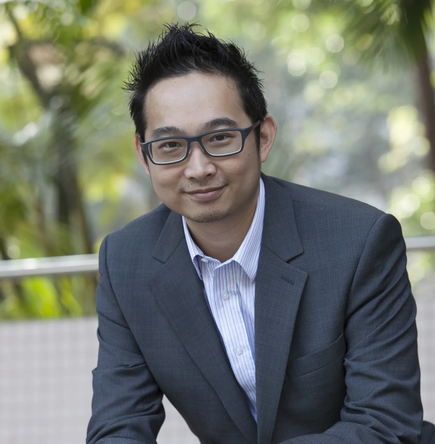 Joe Tang in a grey suit and pale shirt with blurred green park background