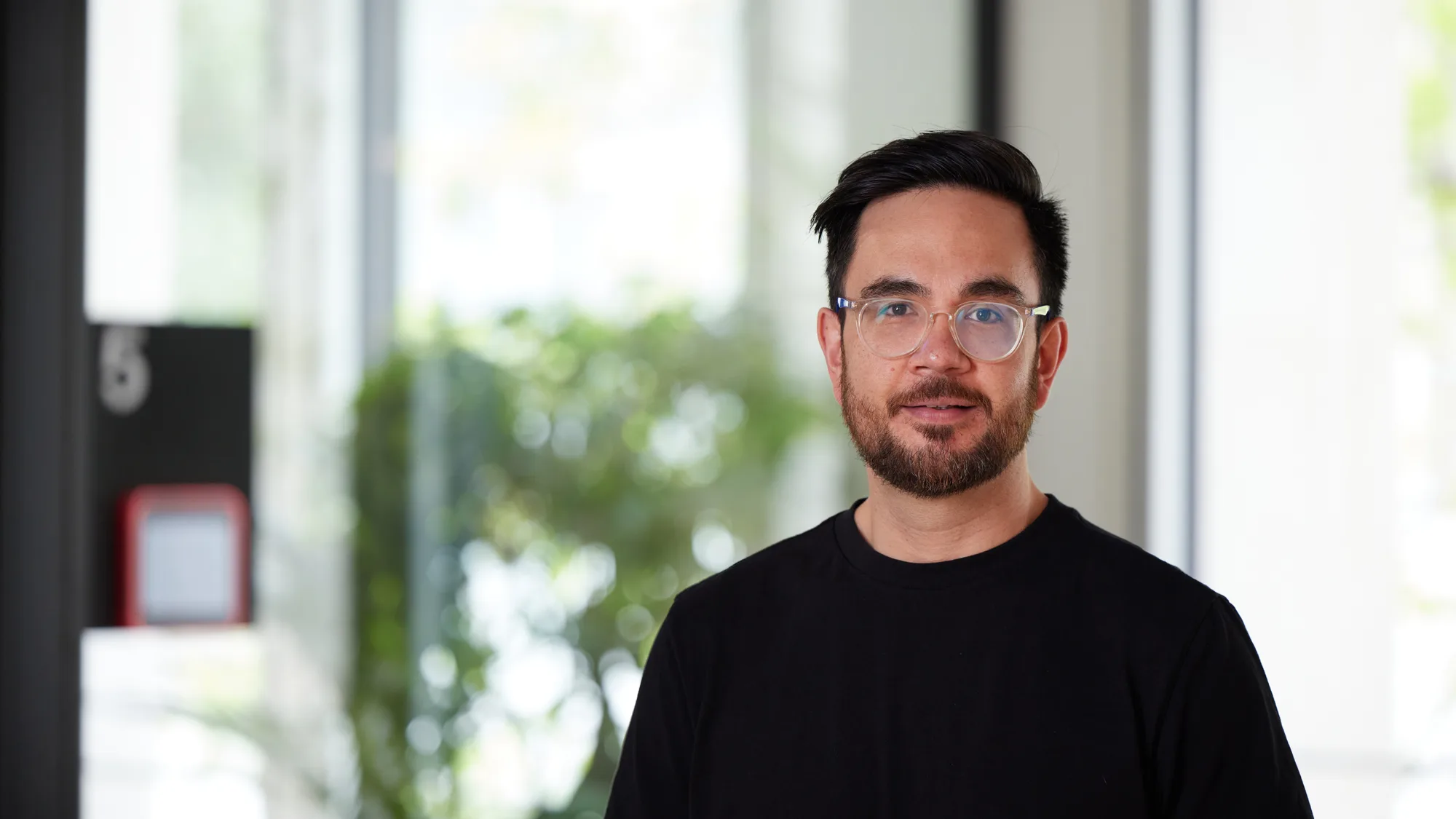 Colin in a dark t-shirt standing in an open plan office area
