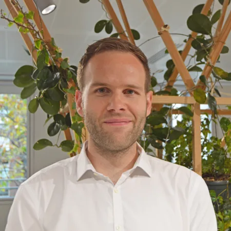 David in a white open collar shirt in front of an interior plant trellis