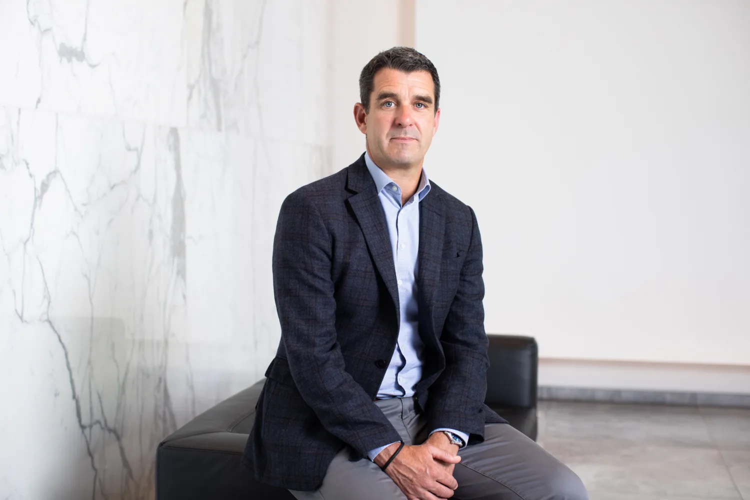 Kevin Hayes in a dark suit jacket sitting in front of a marble wall