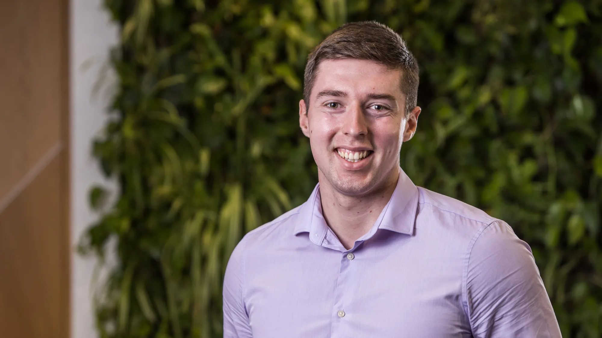 Niall Conyers head and shoulders image while wearing a lilac shirt in front of a greenery backdrop