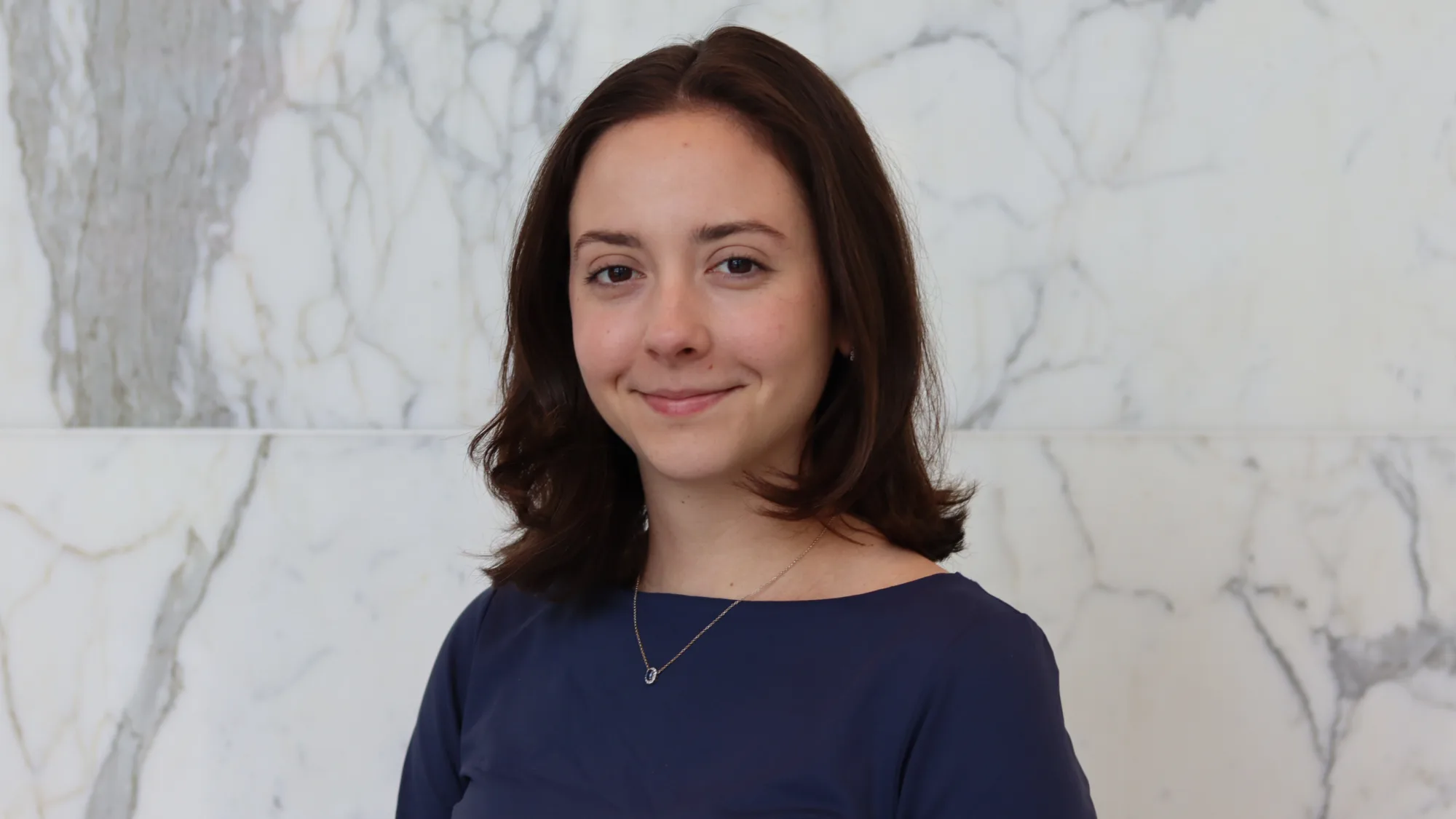 Pauline in a dark blue top in front of a white marble effect wall