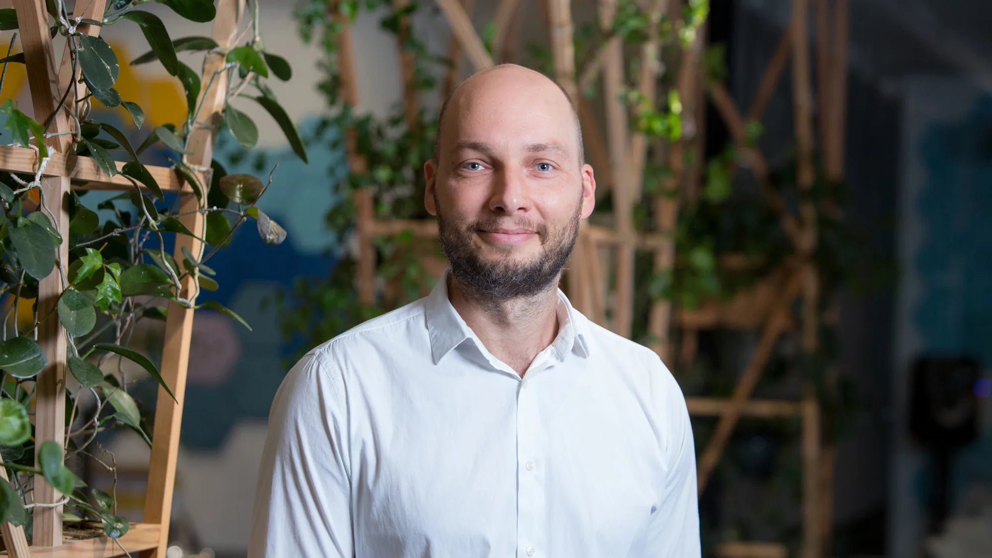 Rytis smiling to camera stood in front of a wooden trellis with plants
