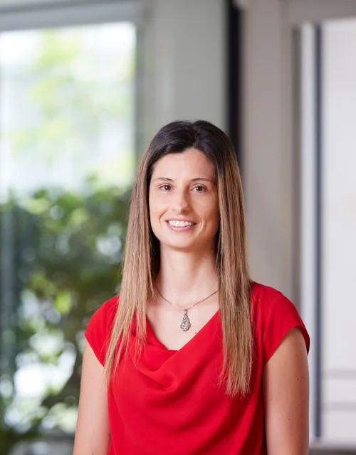 Valeria Riso smiling towards the camera in a red top against a blurred background of the London office