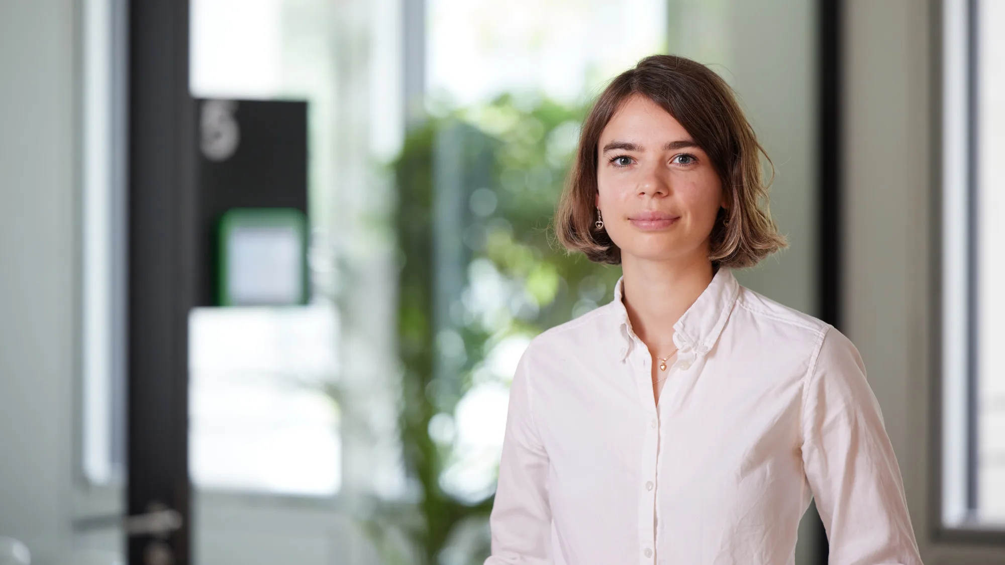 Vera Sehlstedt in a white shirt standing against a blurred background in the London office