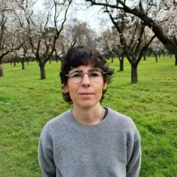 Head and sholders shot of Lucia wearing a grey jumper agaist a back drop of trees
