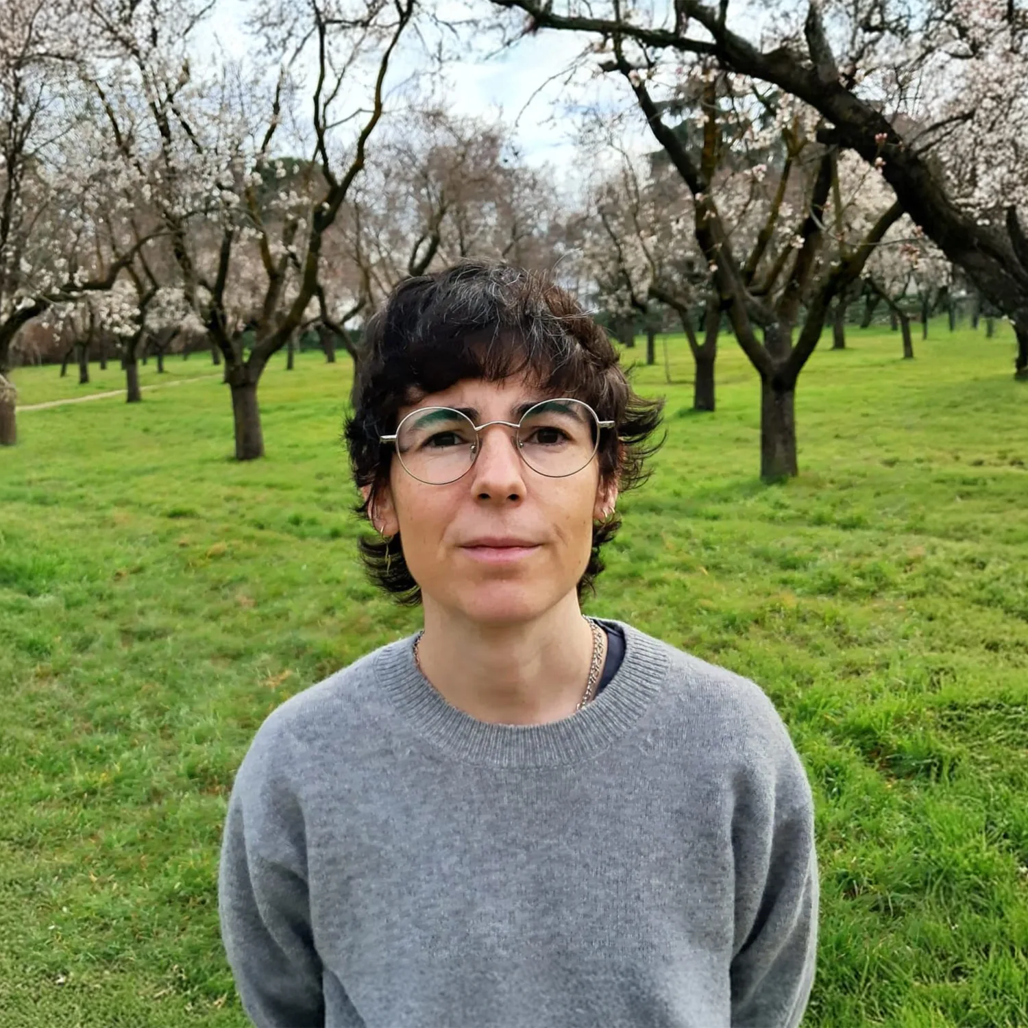Head and sholders shot of Lucia wearing a grey jumper agaist a back drop of trees