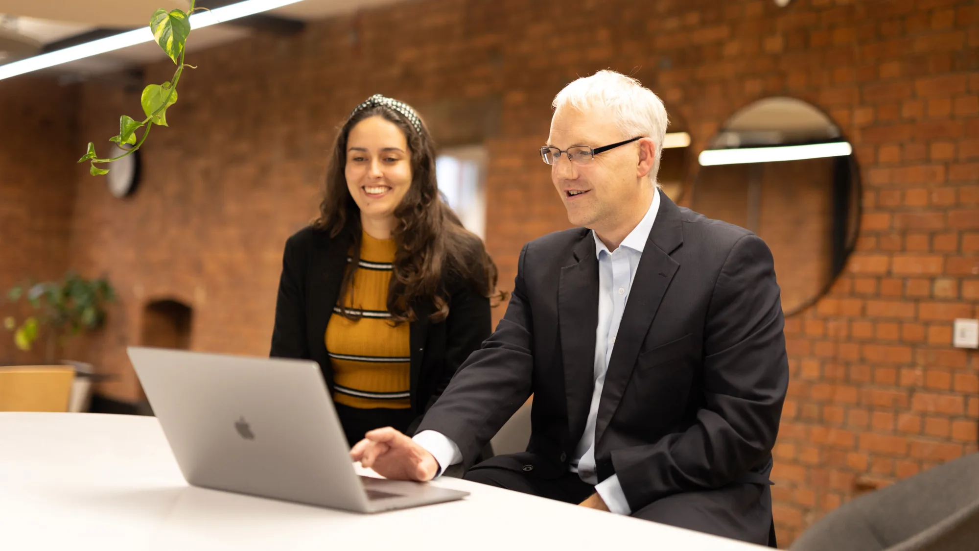 Graham Barker in office hot desk meeting area discussing with colleague and a laptop