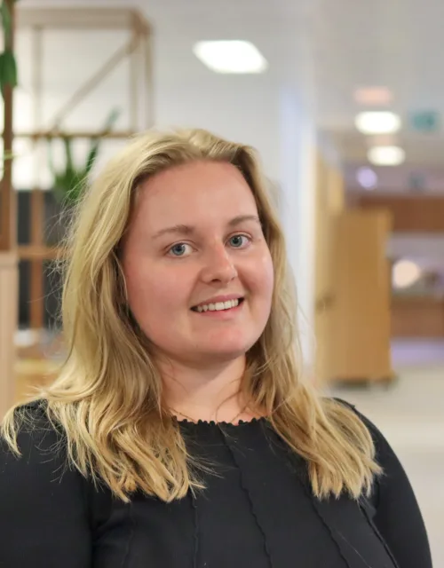 Lauren in a dark top standing in an open plan office