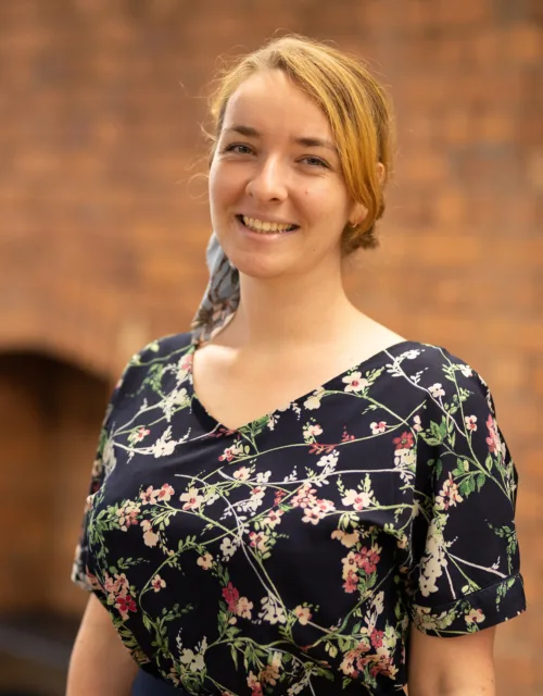 Ola in a short sleeved top stood in front of a brick office wall