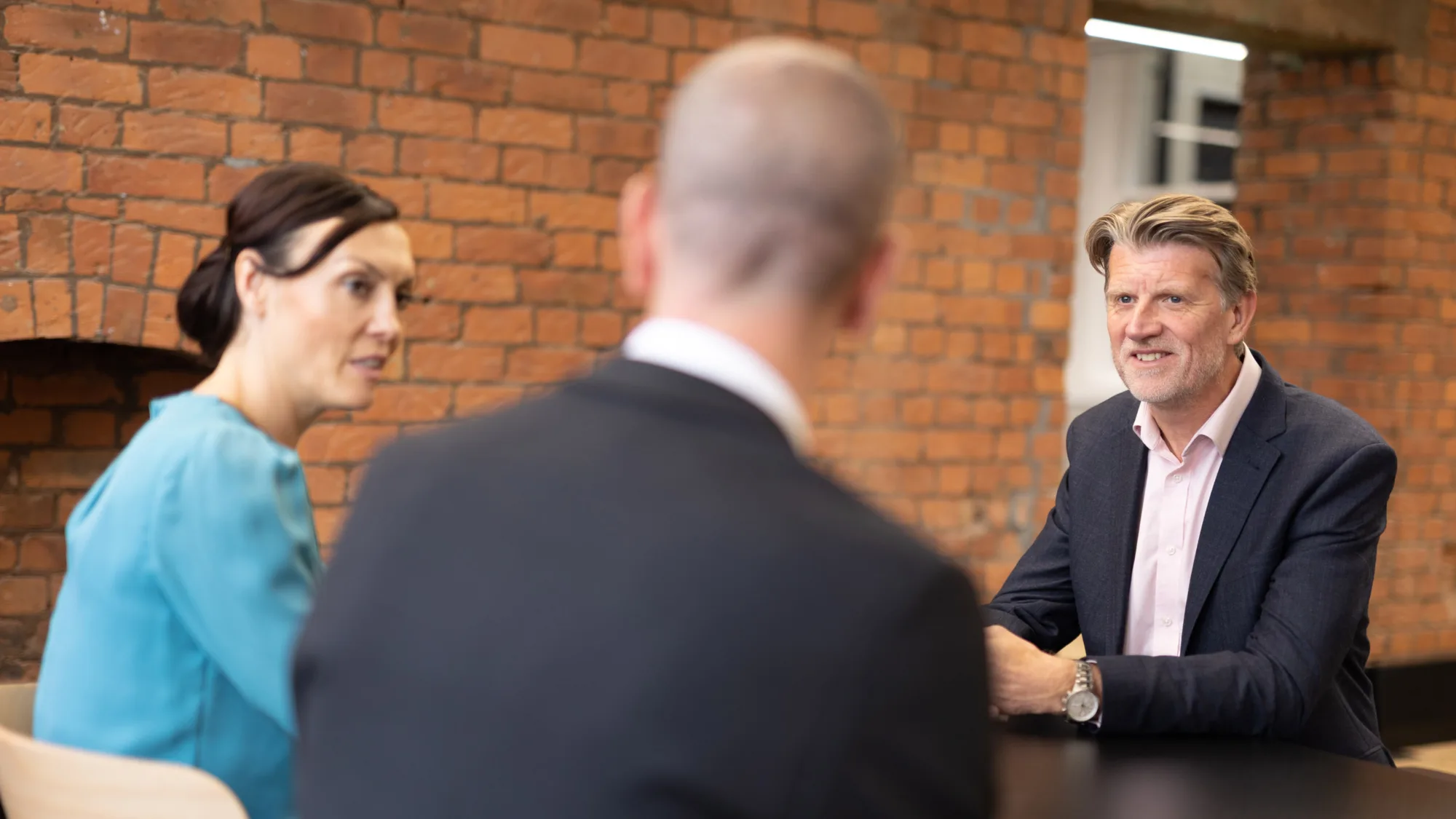 Paul Kenyon in a meeting room with colleagues and brick background