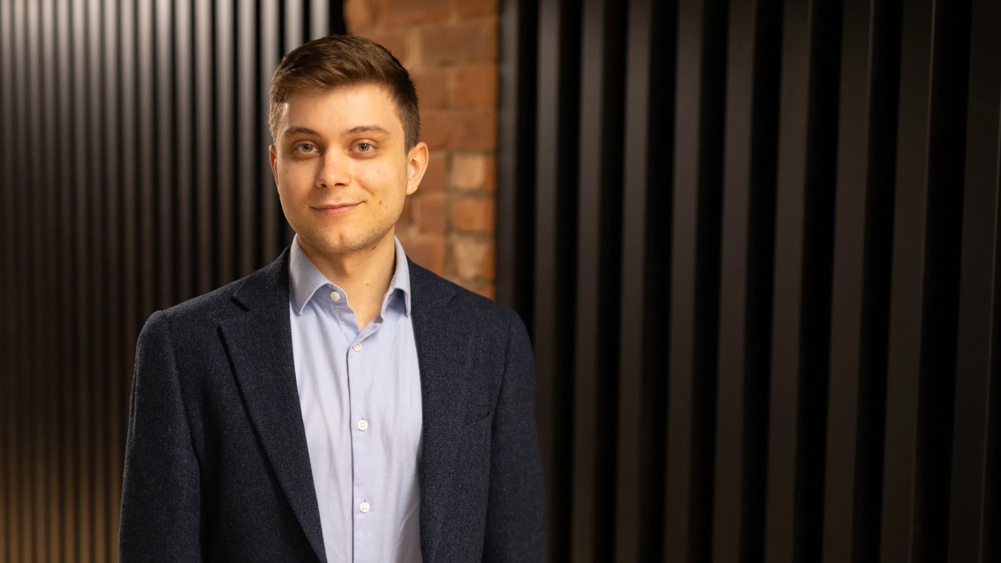 Teodor stood in front of a dark wood panel and brick wall