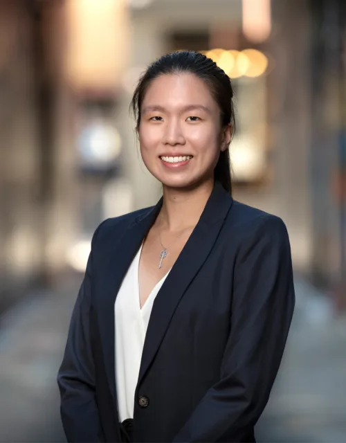 Jocelyn Choy standing in a blazer and white blouse, the background is a blurred street