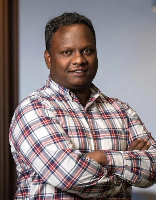 Headshot of Priyatharsan taken inside office with blurred background showing office interior and lighting.