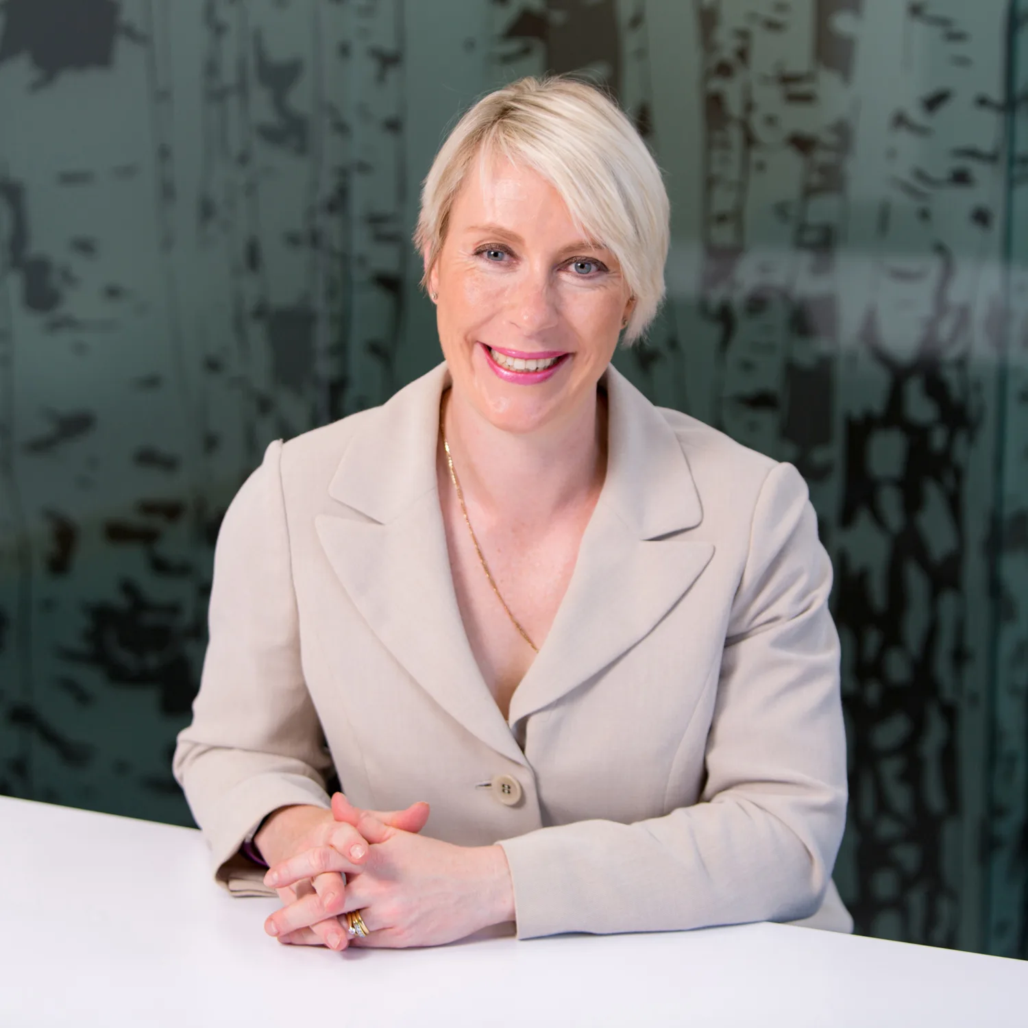 Carole O'Neil in a beige suit at the desk with glass background
