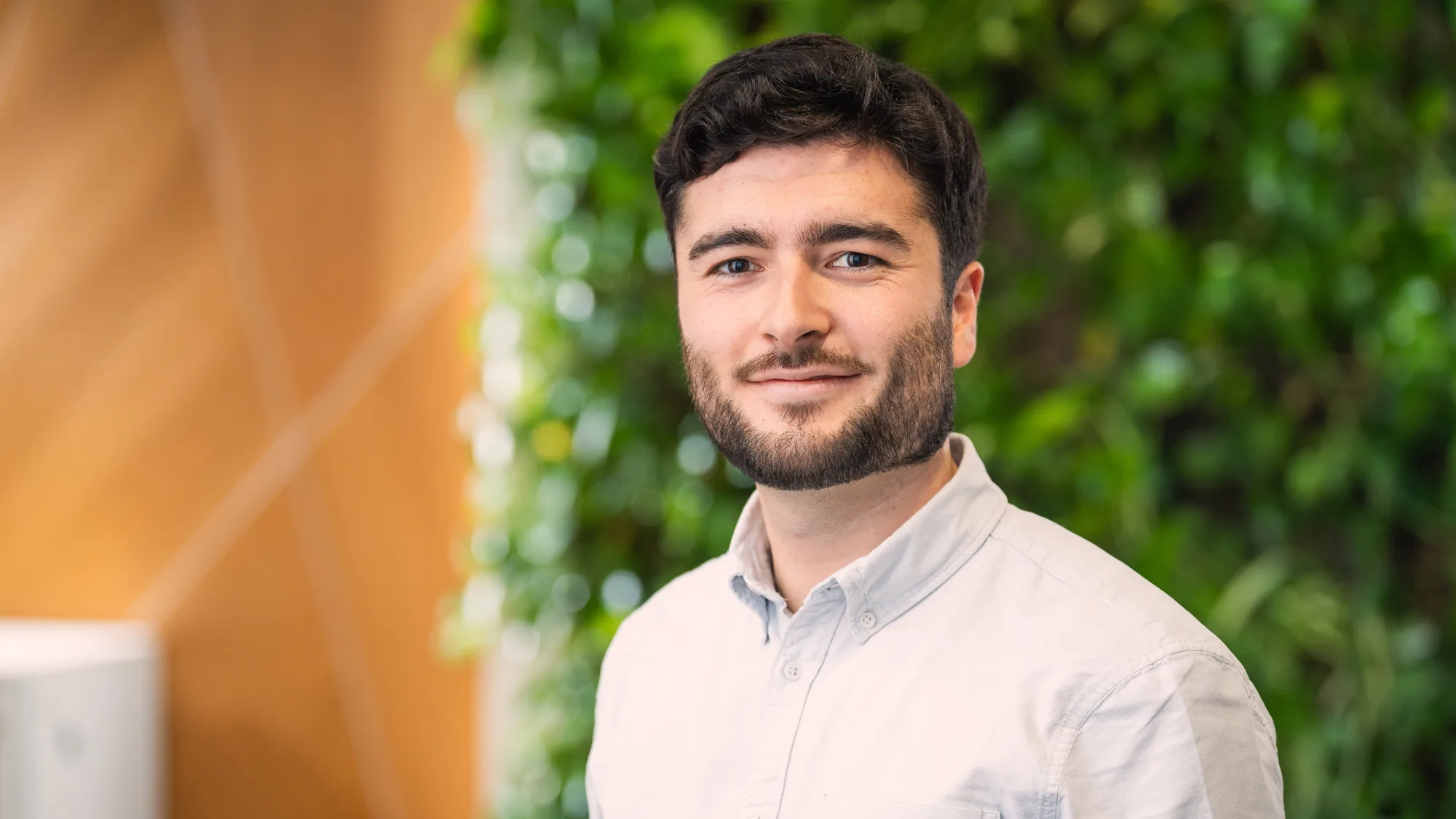 Head and sholders shot of Fergus wearing a pale shirt against a green foliage and wood background