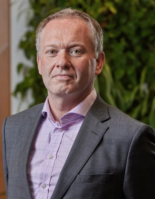 Jim Allen in a grey suit and pink shirt on a wooden panelling and a living wall background