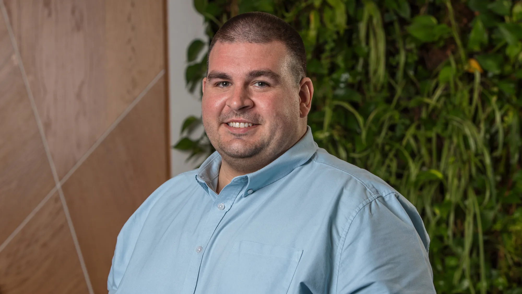 Michael in a light green open collar shirt smiling in front of a living wall