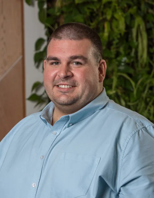 Michael in a light green open collar shirt smiling in front of a living wall