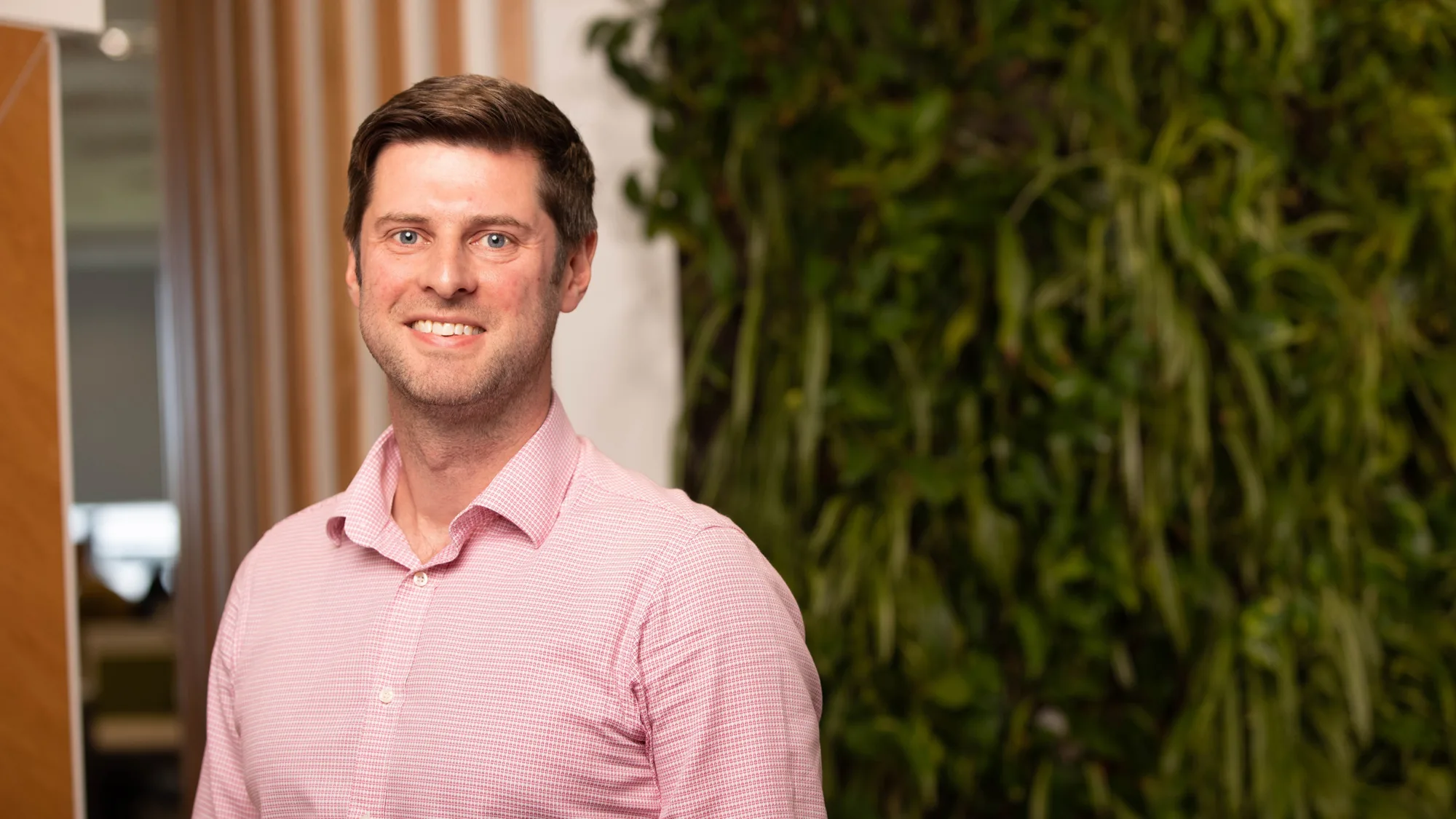 Michael in a pink open collar shirt in front of a living wall