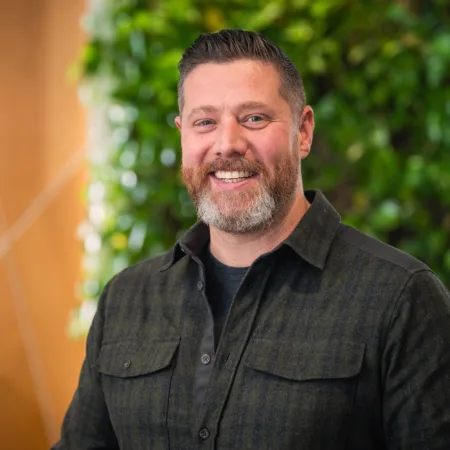 Head and shoulders shot of Oliver wearing a dark shirt against a green and brown background