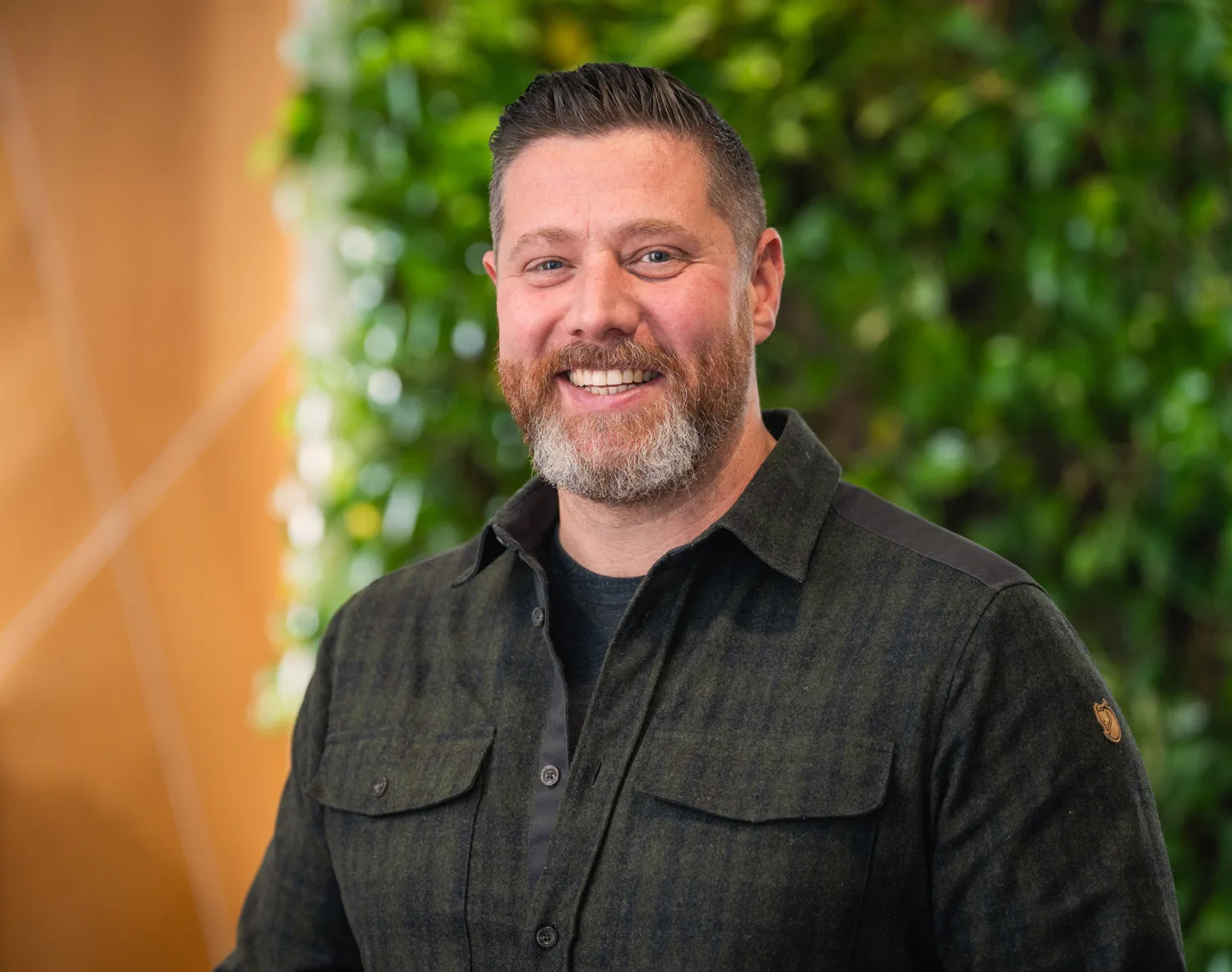Head and sholders shot of Oliver wearing a dark shirt against a green and brown background