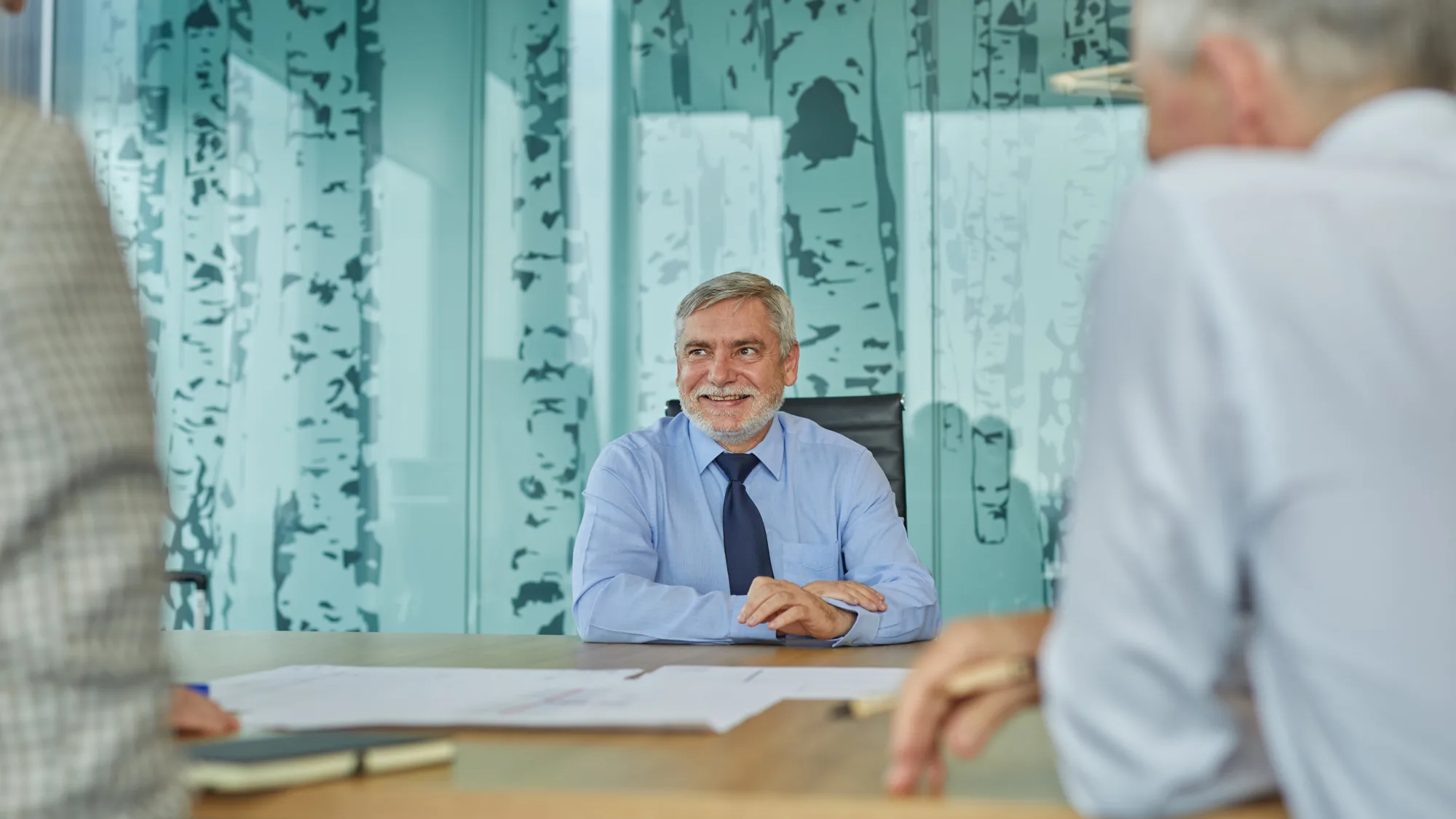 Paul Hards in a meeting with drawings on the table and bamboo glass panelling behind