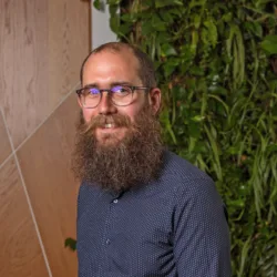 Steven in a dark blue shirt in front of a wooden panel and green living wall