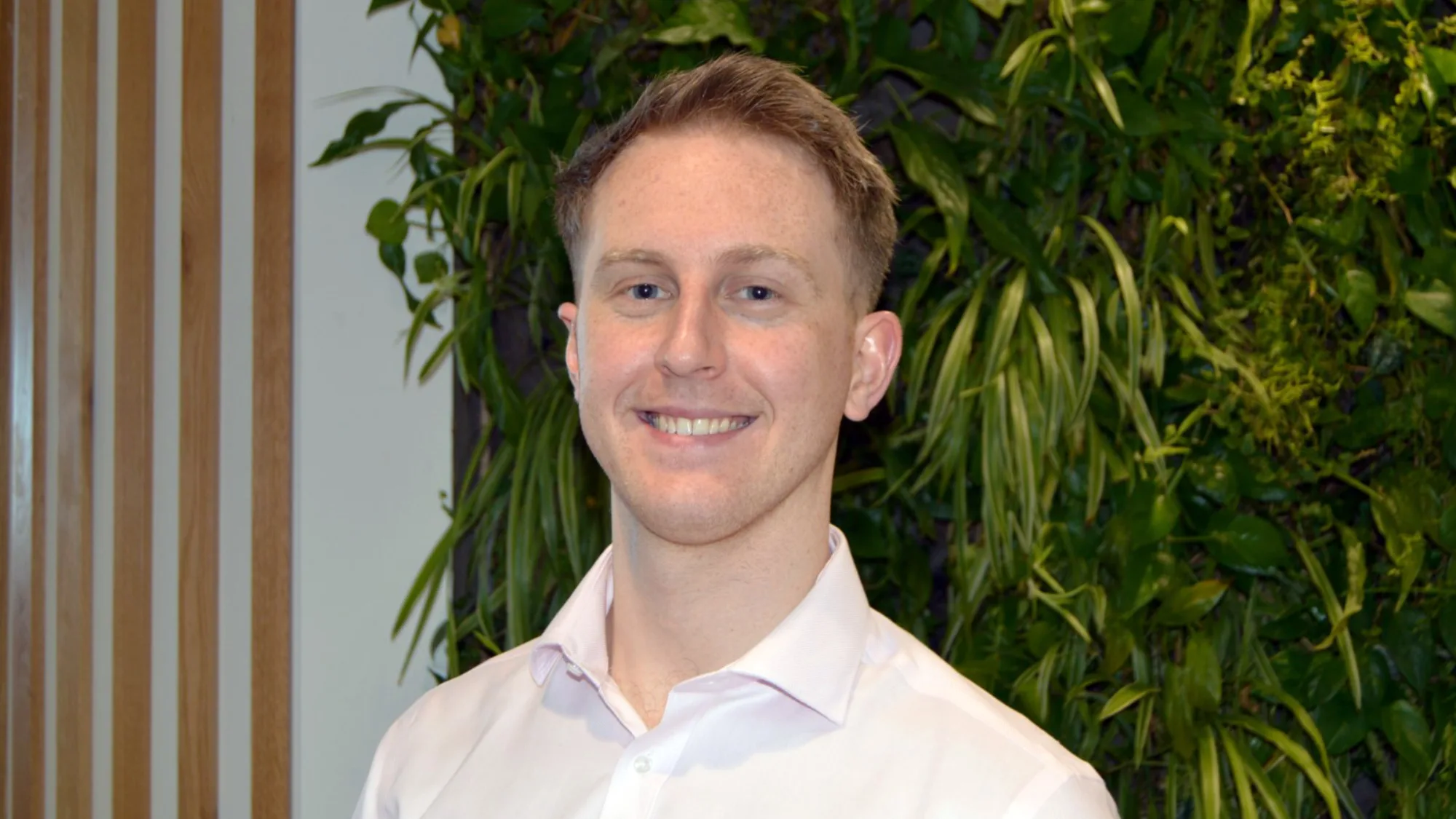Tom in a white open collared shirt in front of a living wall