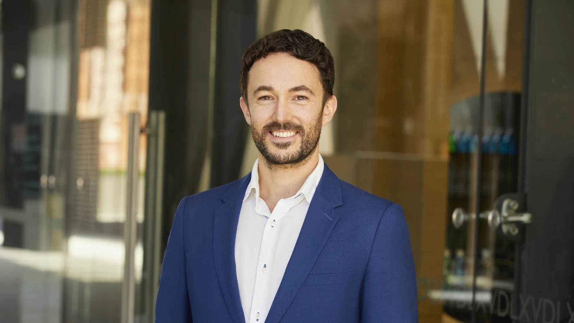 Oliver Grimaldi in suit in front of office entrance glass doors