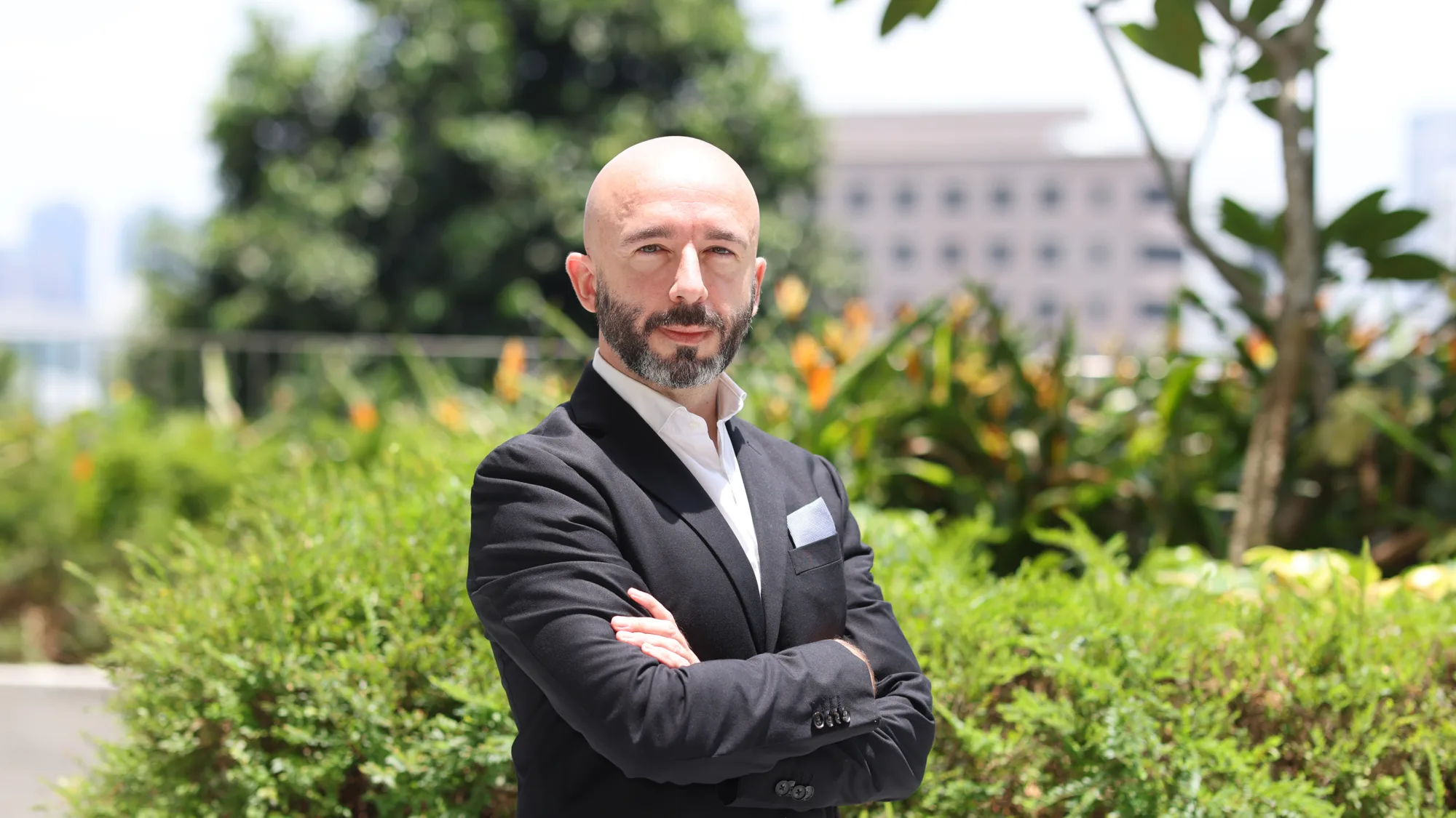 Alex Saez, arms folded, outdoors in front of greenery