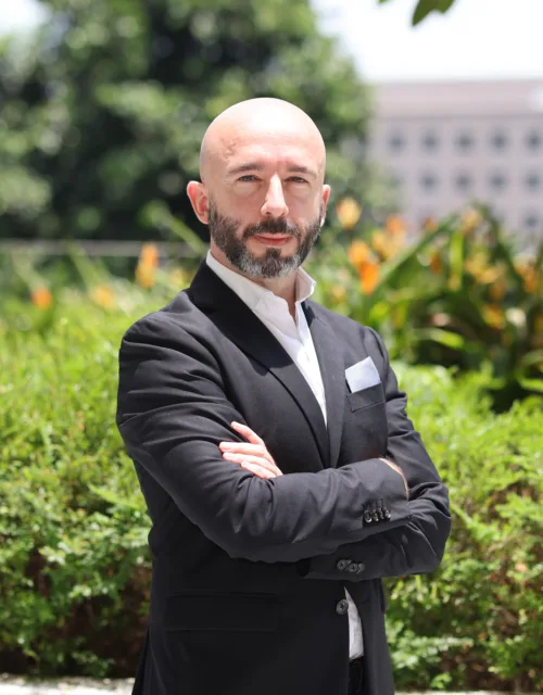 Alex Saez, arms folded, outdoors in front of greenery