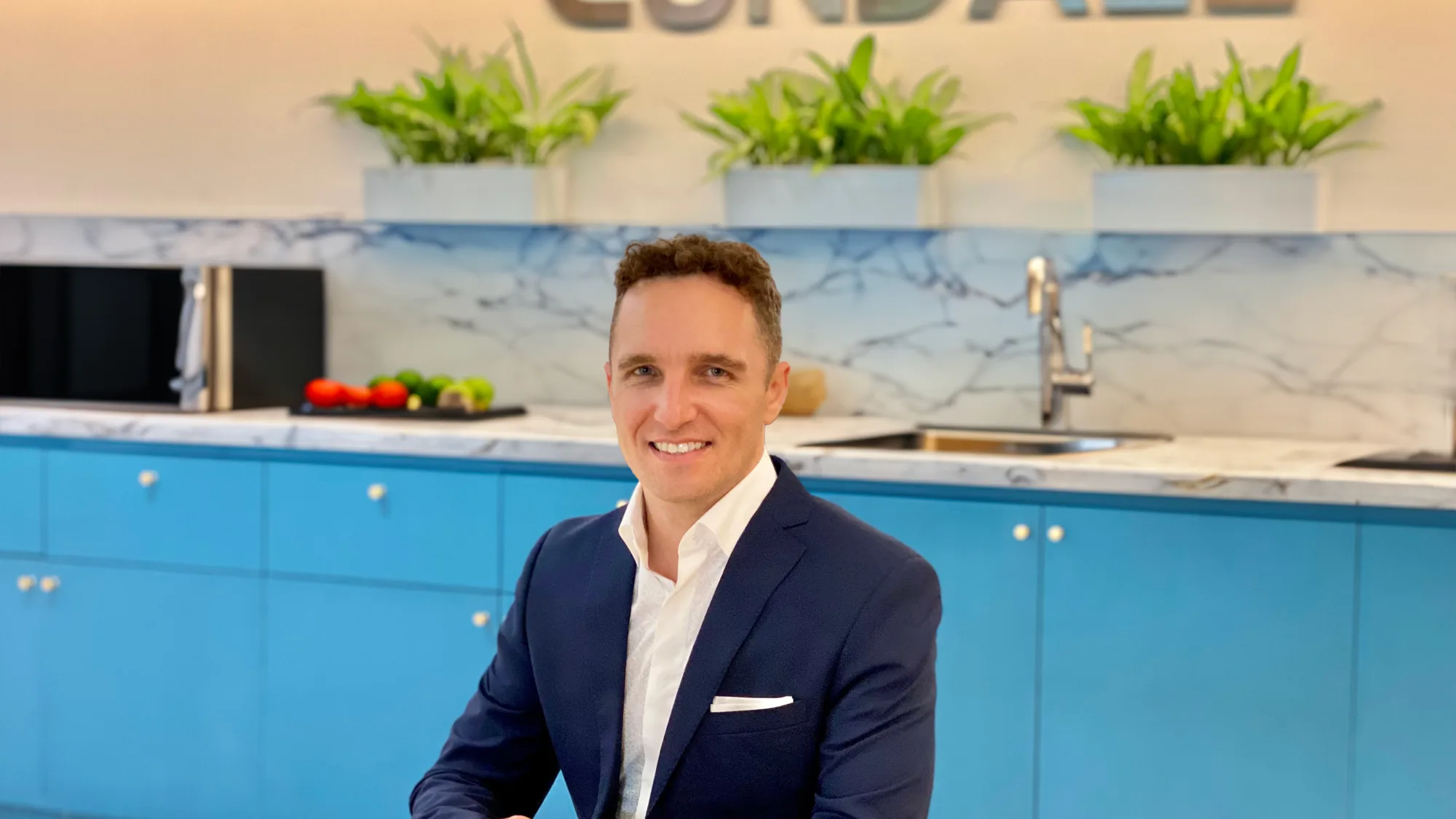 Matt sat with arms resting on a long table with a kitchen in the background and Cundall logo on the wall