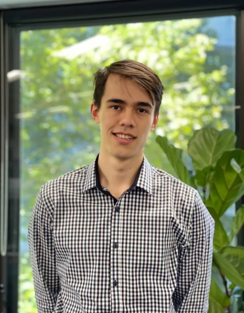 Head and shoulders shot of Richard wearing checked shirt standing in front of greenery