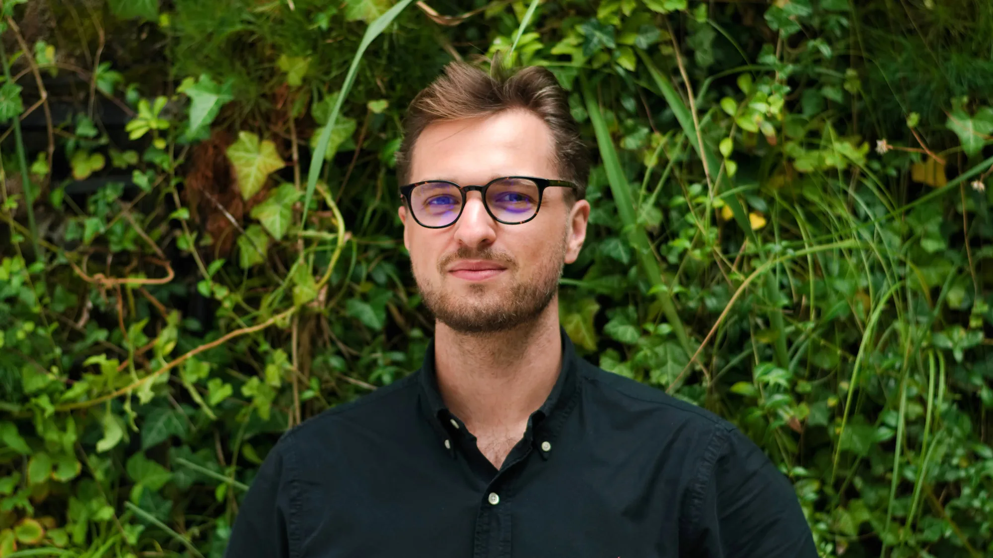 Igor in a dark open collar shirt in front of a living wall
