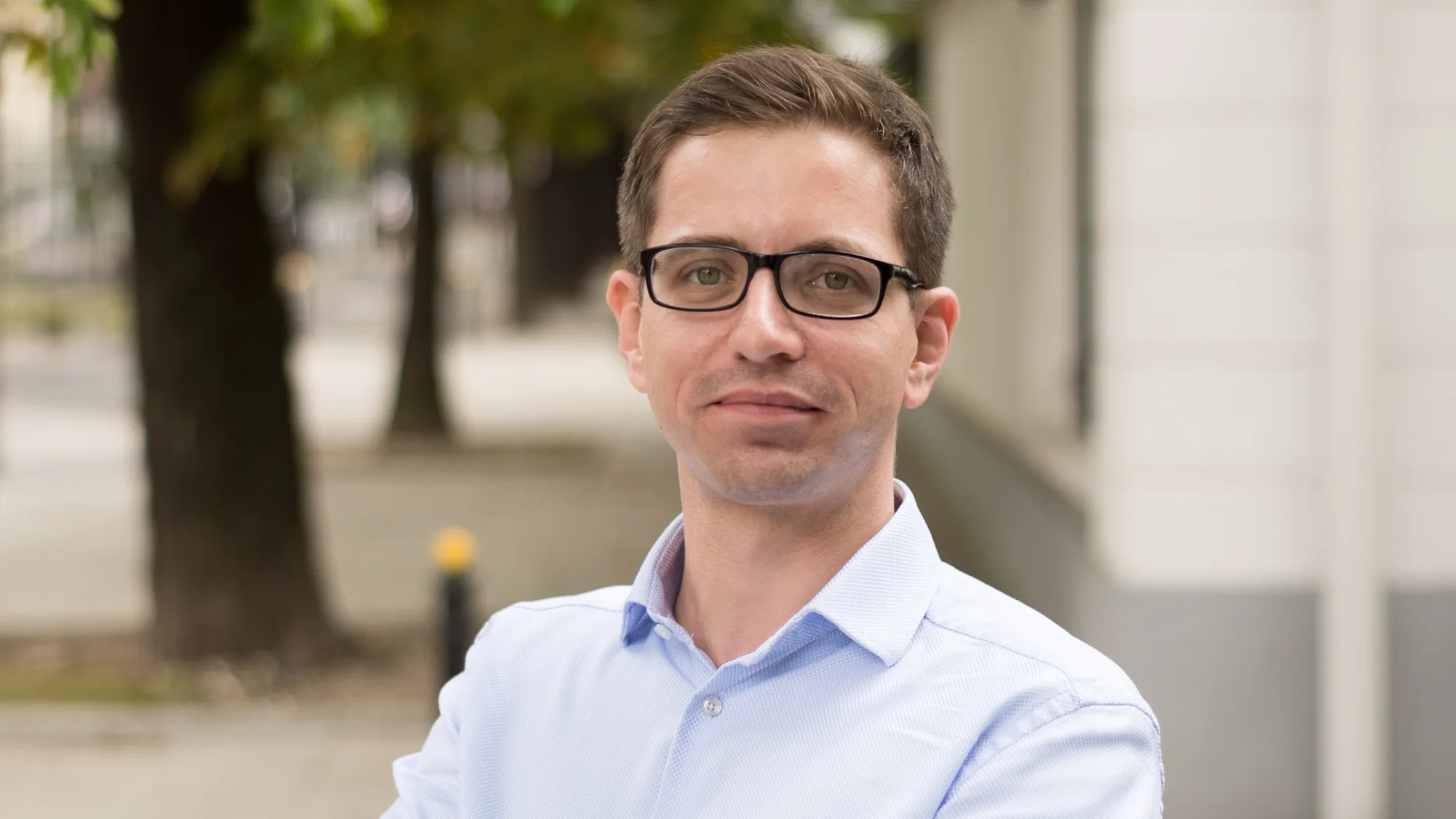 Kamil Feret looking towards the camera wearing a light blue shirt against a blurred background of a street