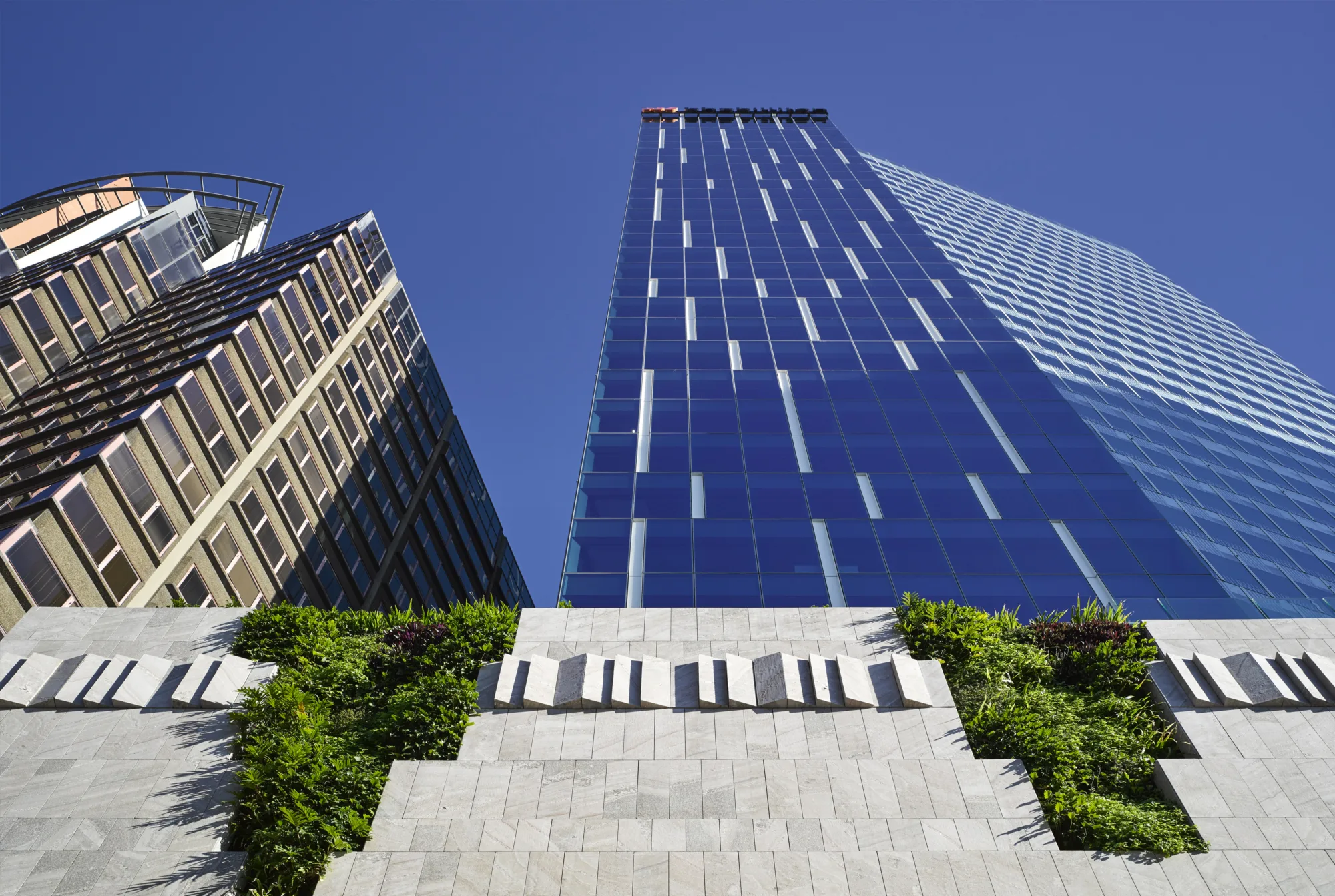Ground view of 480 Queen street towering into the blue sky with the buildings exterior reflecting the blue around it.