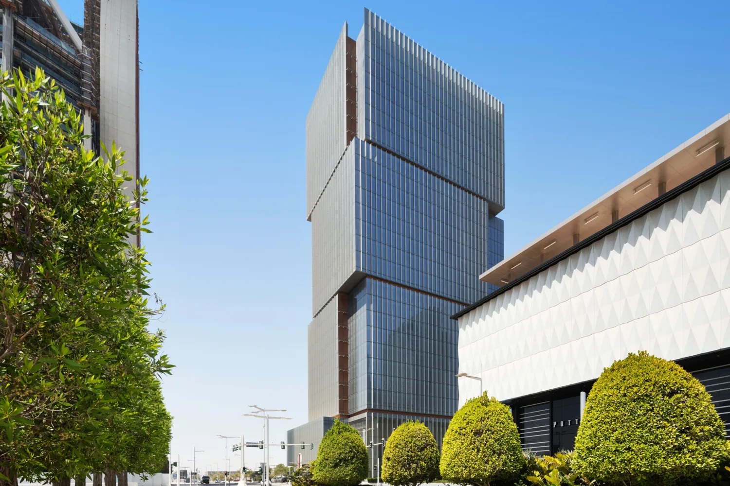 Angled view of a modern glass tower with unique design features; foreground includes trees and landscaped elements.