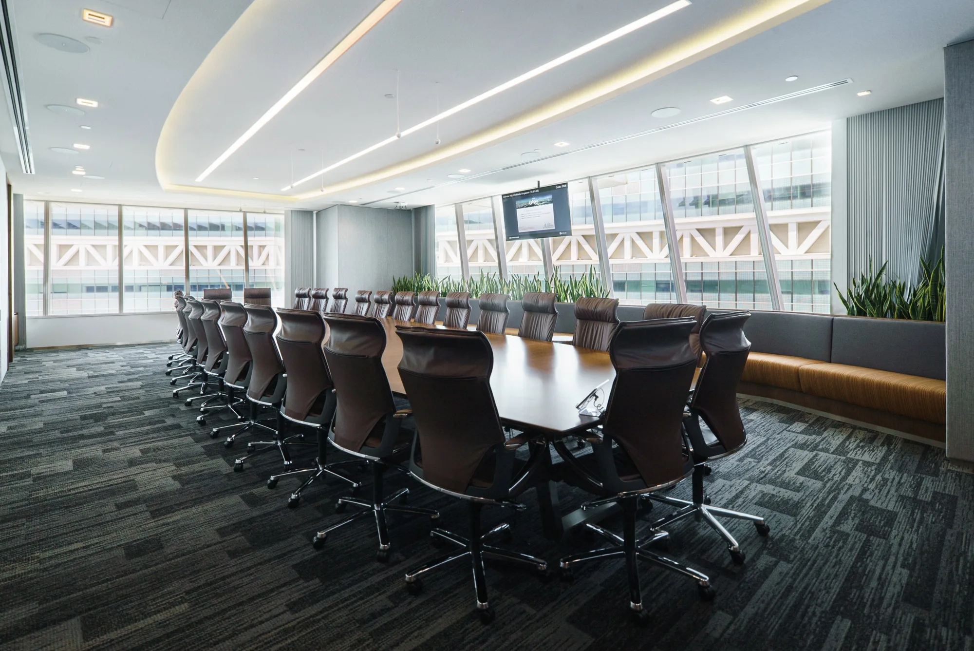 Large meeting room with long wooden table lined with office chairs and surrounded by glass panel windows allowing natural light in